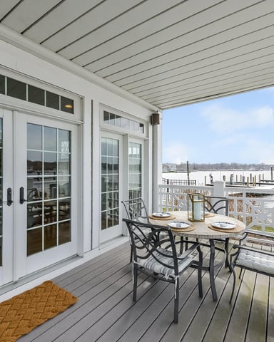 Waterfront deck with dining table, chairs, white pergola, glass doors, and bay view with docked boats