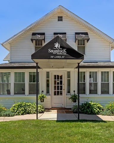 White two-story inn with black awning, large front windows, and landscaped garden entrance on sunny day