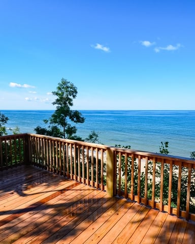 Wooden deck with railing overlooking calm blue lake and tree-lined shoreline under clear sky