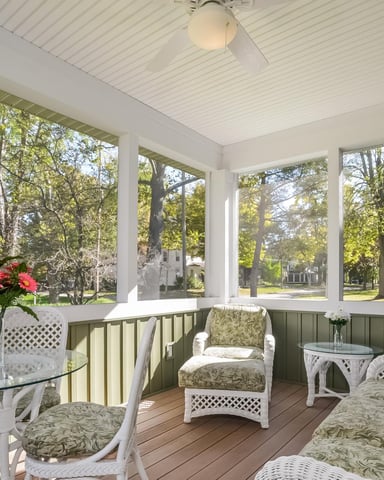 Screened porch with white wicker furniture, green cushions, and views of tree-lined street