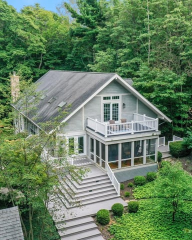 Modern two-story house with white siding and dark roof surrounded by dense green forest and landscaped grounds.