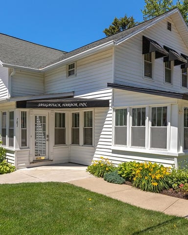 White farmhouse with black awnings, large windows, and landscaped front yard under clear blue sky