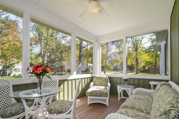 Screened porch with white wicker furniture, green cushions, and views of tree-lined street