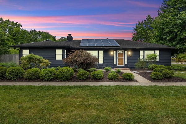 Modern dark-sided ranch house with solar panels, manicured landscaping, and lawn at sunset