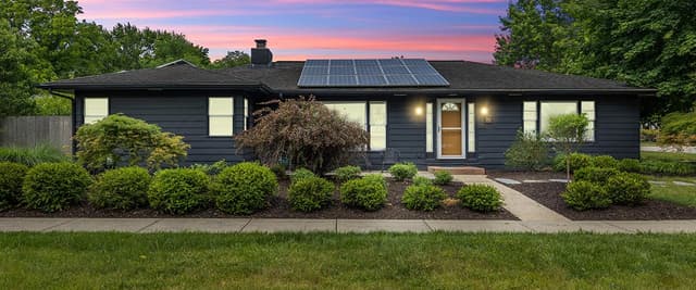 Modern black ranch house with solar panels, landscaped front yard, and sunset sky